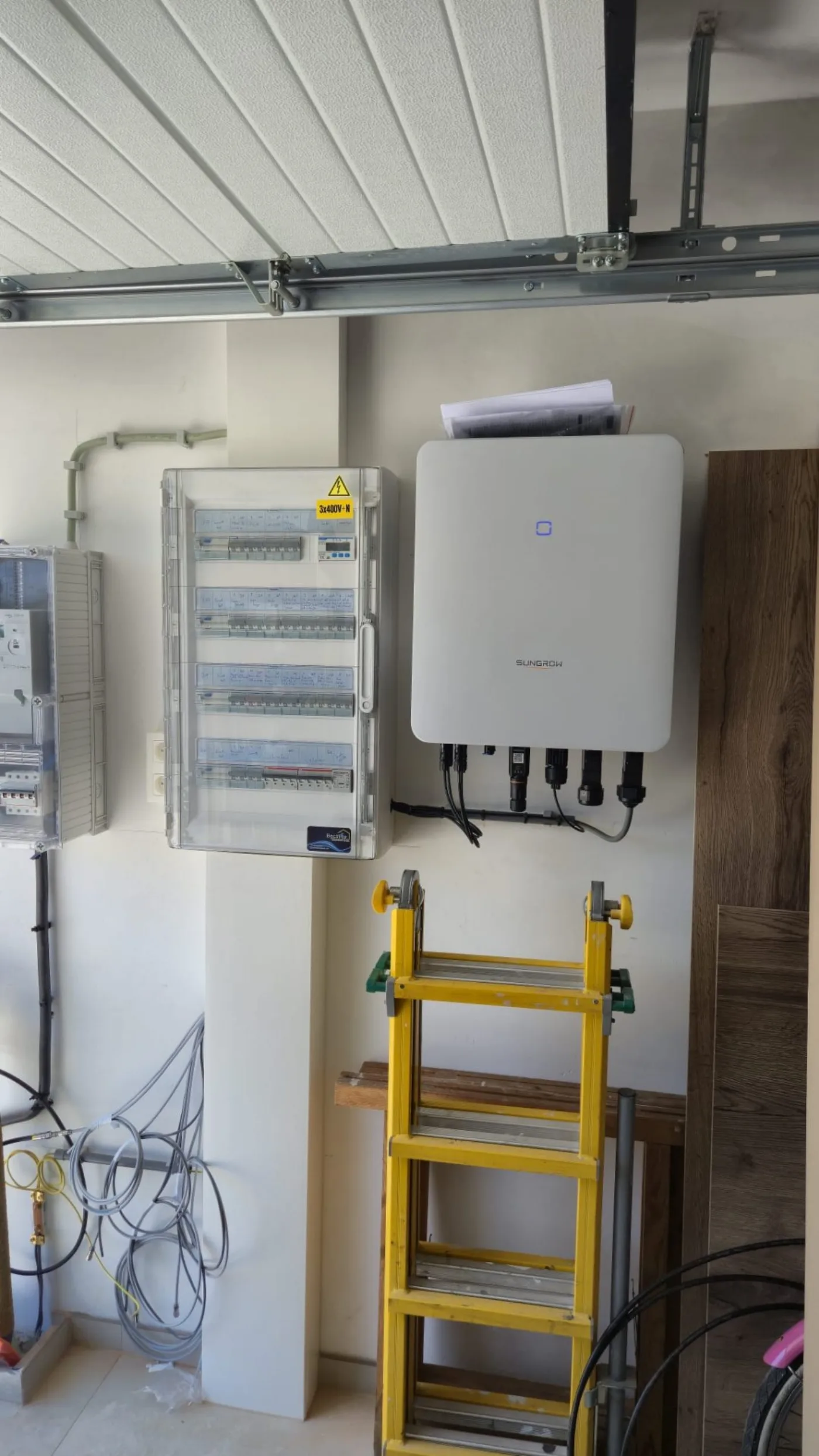 Onduleur hybride Sungrow 10 kVA avec backup intégré installé dans un garage à Soignies, à côté d'un tableau électrique triphasé 3x400V+N