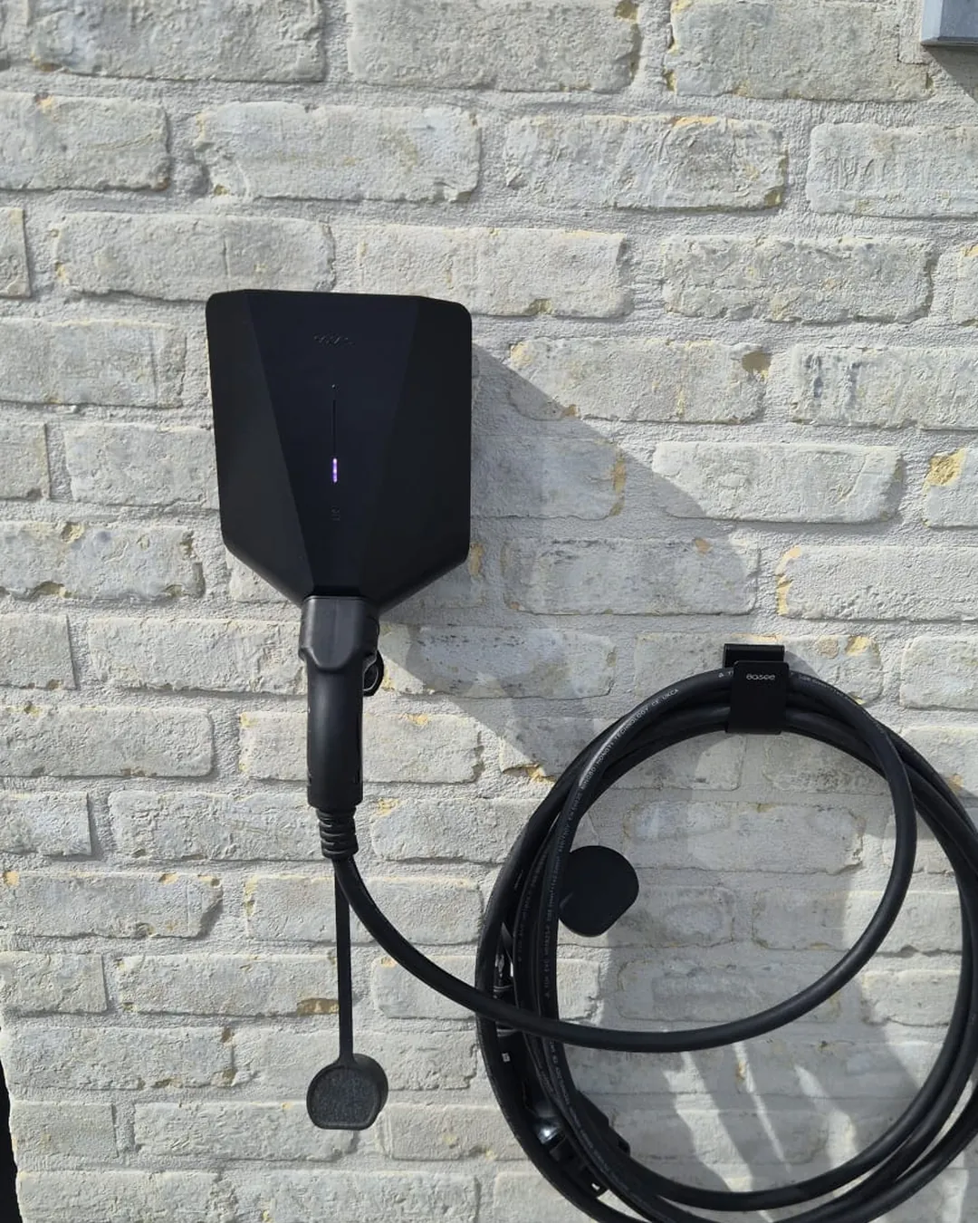 Borne de recharge Easee 22 kW noire installée en façade brique claire à Naast, câble Type 2 lové sur support mural