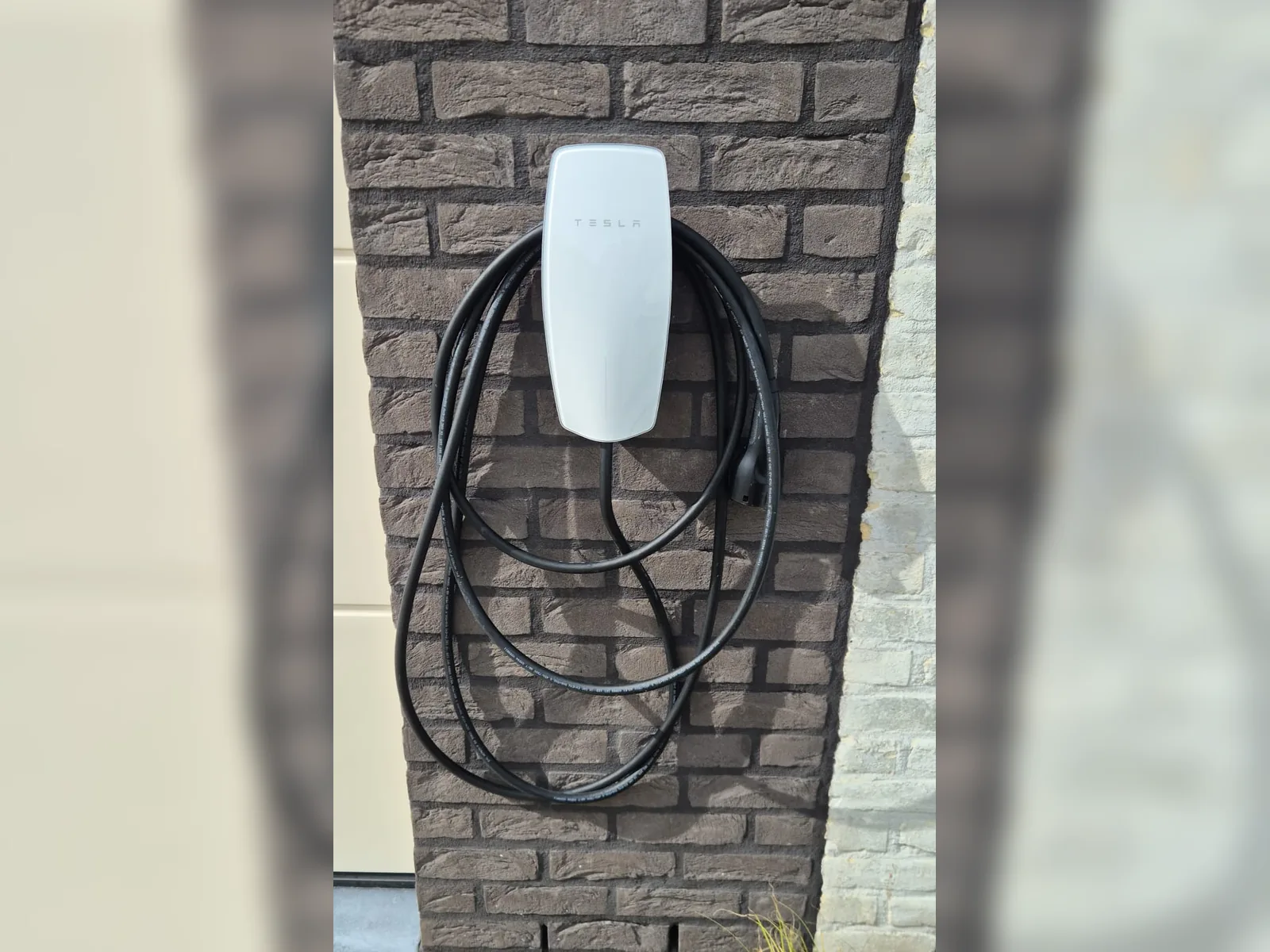 Borne de recharge Tesla Wall Connector 22 kW blanche installée en façade brique foncée à Neufvilles, câble Type 2 attaché à la wallbox